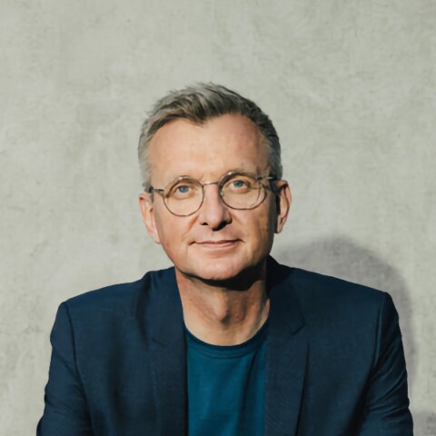 Headshot portrait of German journalist Jochen Wegner, looking at the camera, sitting in front of a grey background.