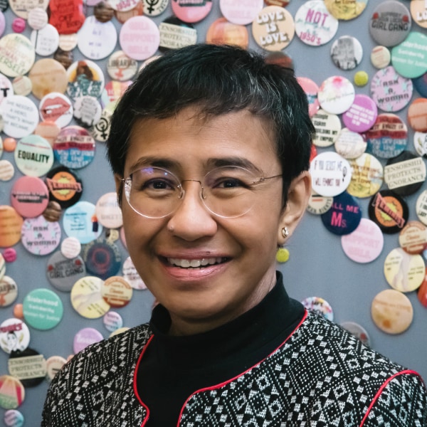 Environmental portrait of Nobel Peace Prize laureate Maria Ressa in front of a colorful wall full of stickers expressing freedom of speech.