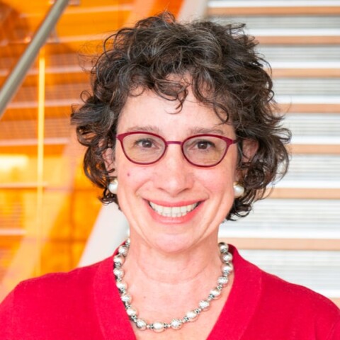 Portrait of Berkeley biologist Jodi Halpern, standing in front of a set of stairs, smiling at the camera.