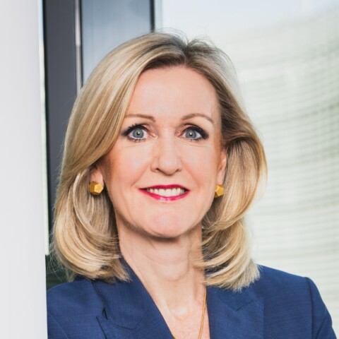 Headshot portrait of Ann Mettler, Breakthrough Energy, standing in front of a window, smiling at the camera.