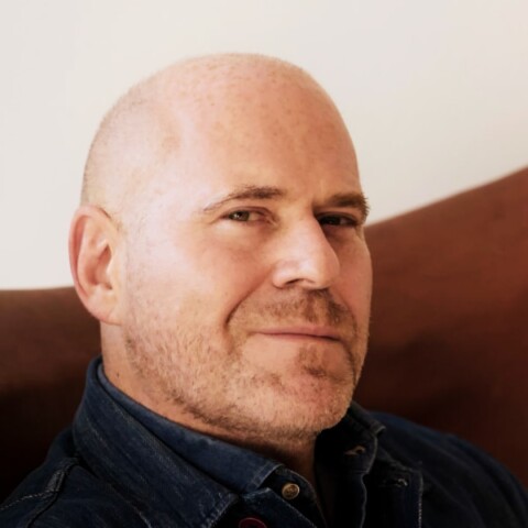 Headshot portrait of art manager Marc Spiegler in front of a beige and red wall.
