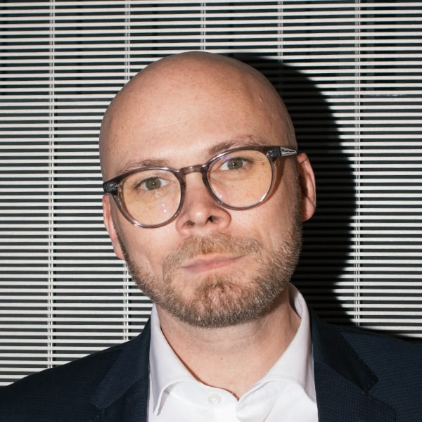 Brightly lit portrait photo of Fabian Mehring, State Minister Bavarian Ministry for Digital Affairs, in front of a striped background with prominent shadow.