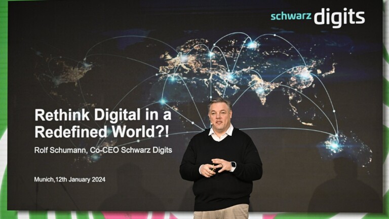 Schwarz Digits CEO Rolf Schumann on stage at the DLD Munich Conference 2024, in front of a video screen showing his presentation.