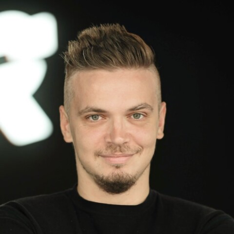 Portrait image of Jack de Santis, founder and CEO of Omira AI, wearing a black t-shirt in front of a black-and-white studio background.