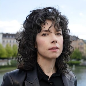 Outdoor portrait photo of Meredith Whittaker, President of the Signal Foundation, wearing a black leather jacket, looking at the camera.