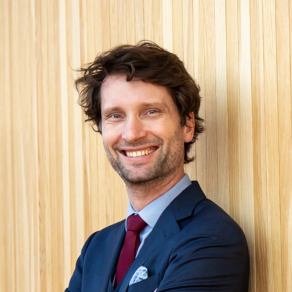 Portrait image of Michal Kosinsk, Professor of Organizational Behavior at Stanford University, wearing a blue suit, smiling at the camera, standing in front of a wooden wall.