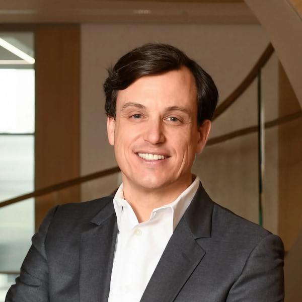 Portrait image of Philipp Freise, Partner at investment firm KKR in London, seen in the lobby of a building with a staircase behind him, wearing a suit and white shirt, smiling at the camera.