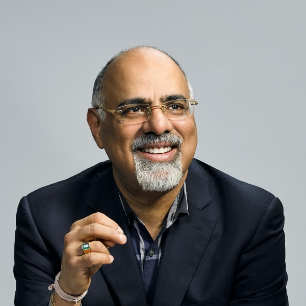 Studio portrait of Raja Rajamannar, Chief Marketing & Communications Officer of Mastercard, seen in front of a grey background, looking right, smiling.