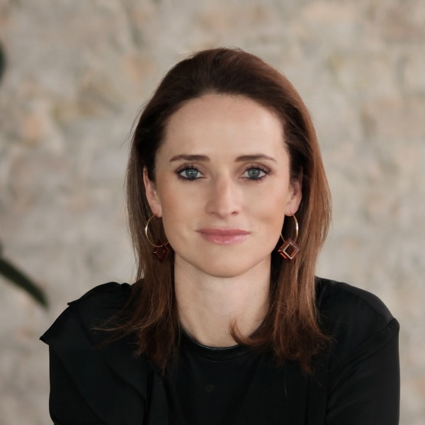 Portrait image of Verena Pausder, Chairwoman of the German Startup Association, in front of a grey wall.