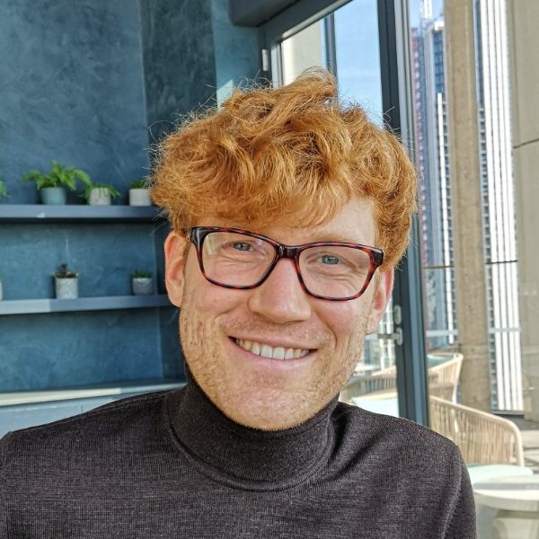 Environmental portrait of Black Forest Labs co-founder Andreas Blattmann, wearing glasses and a black turtleneck sweater, smiling at the camera.