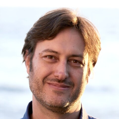 Outdoor portrait of Daniel Barcay, Executive Director of the Center for Humane Technology, looking at the camera in front of a blurry blue background.
