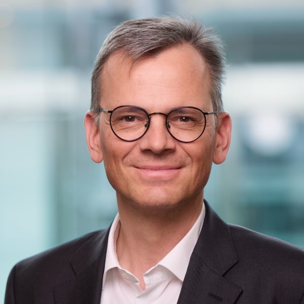 Indoor portrait of SAP manager Dominik Asam, wearing a suit and glasses, smiling at the camera.