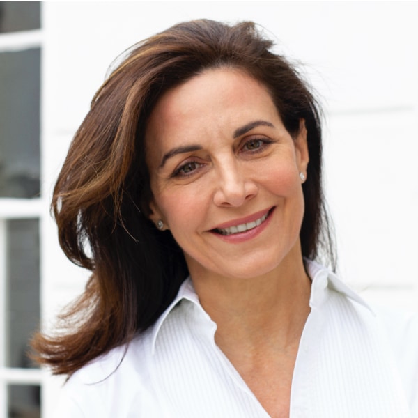 Outdoor portrait of entrepreneur, investor and advisor Fabienne Serfaty, wearing a white blouse, standing in front of a building.