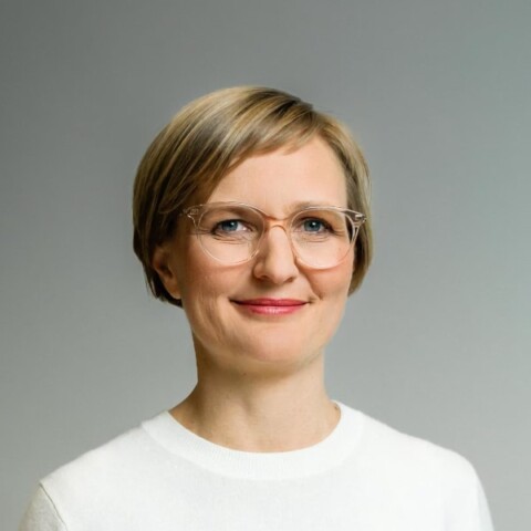 Studio portrait of German politician Franziska Brantner in front of a neutral grey background, smiling at the camera.