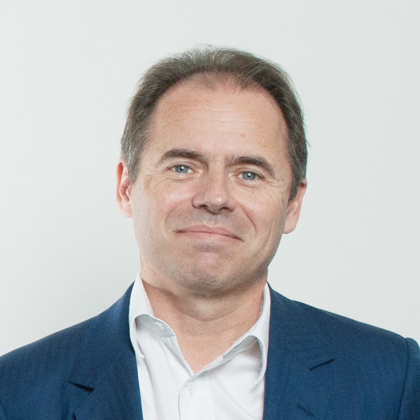 Headshot portrait of FinalSpark CEO Dr. Fred Jordan, seen wearing a blue suit, smiling at the camera, in front of a clean grey background.