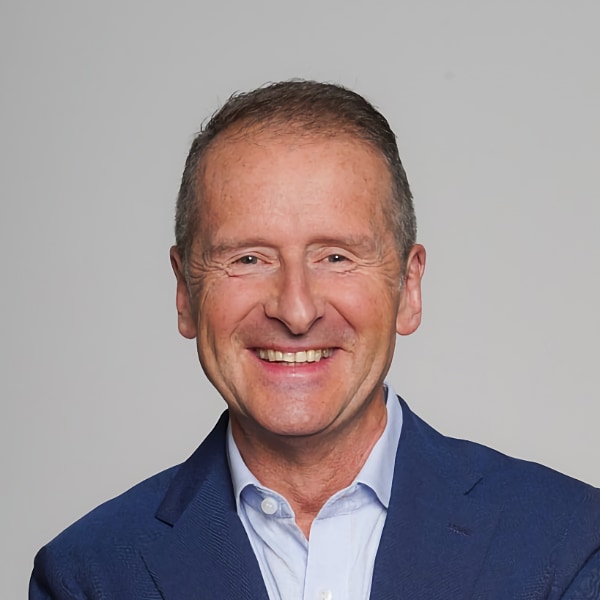 Studio portrait of German manager Herbert Diess (Infineon, VW) in front of a neutral grey background, smiling at the camera.