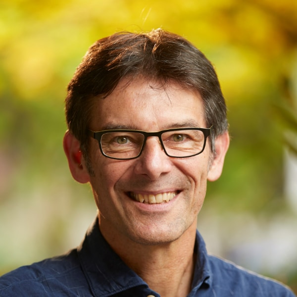 Outdoor portrait of biologist Martin Wikelski, founding Director of the Max Planck Institute of Animal Behavior, in front of a colorful, blurry background.