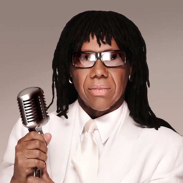 Studio portrait of famed musician and producer Nile Rodgers, wearing glasses, holding a microphone.