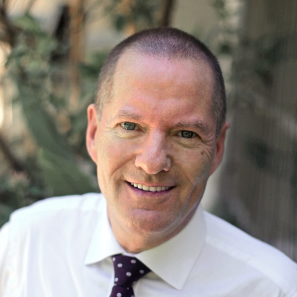 Outdoor portrait of Shai Reshef, President of University of the People, wearing a white shirt and tie, smiling at the camera.