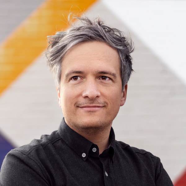 Portrait of Thorsten Heilig, Founder and CEO of Paretos, looking left, wearing a black shirt in front of a colorful pattern background.