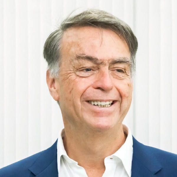 Headshot portrait of André Hoffmann, Vice Chairman of Roche, smiling, looking to his left, standing in front of a neutral grey background.