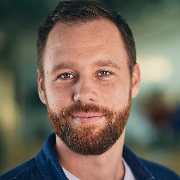 Tightly cropped headshot portrait of Christian Brix Tillegreen, Director of the Planetary Health Team at the BioInnovation Institute, seen in front of a colorful, blurred background, smiling at the camera.