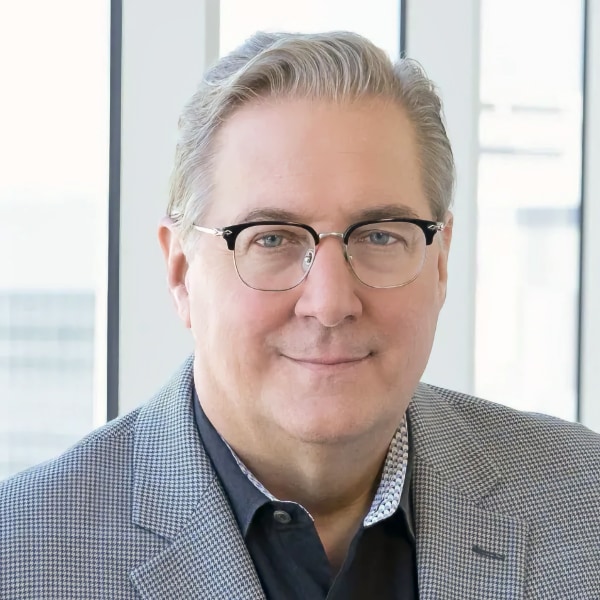 Headshot portrait of Intel CTO Greg Lavender, wearing a grey suit, looking at the camera, standing in front of a window.