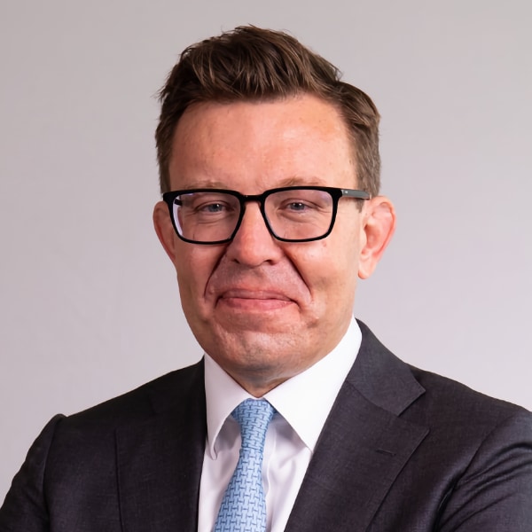 Studio headshot portrait of Brunswick Group CEO Henry Timms, wearing a suit, smiling at the camera.