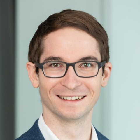 Headshot portrait of McKinsey partner Jakob Stöber in front of a grey background, smiling at the camera.