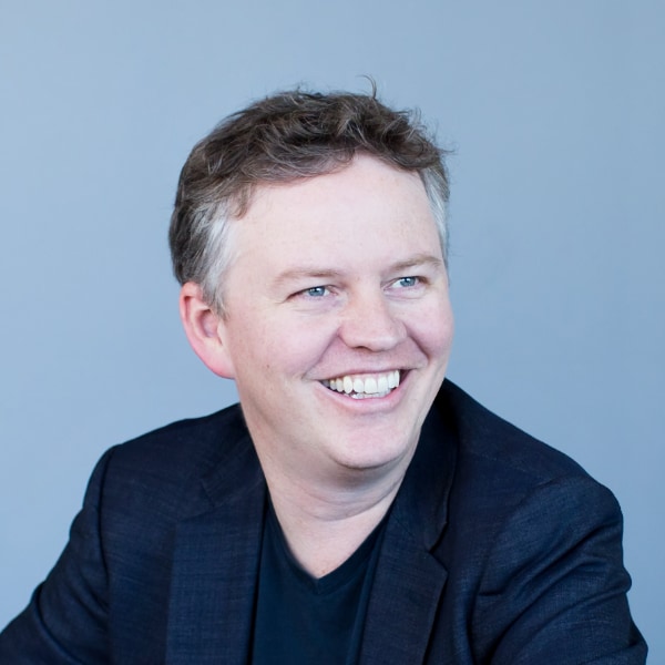 Studio portrait of Cloudflare co-founder and CEO Matthew Prince, sitting in front of a blue background, looking over his left shoulder out of the frame.