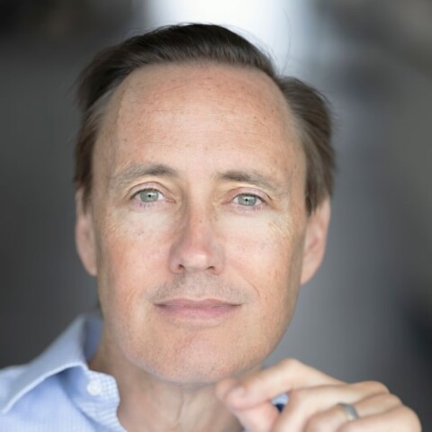 Headshot portrait of famous venture investor Steve Jurvetson, smiling at the camera in front of a bokeh-blurry background.