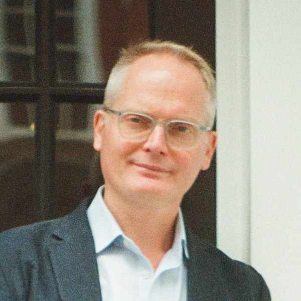 Grainy headshot portrait of author and music industry expert Will Page, wearing a suit, standing in front of a door.