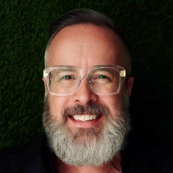 Headshot portrait of Strangeworks founder William Hurley, better known as Whurley, seen smiling at the camera, wearing white-rimmed glasses and a grey beard.