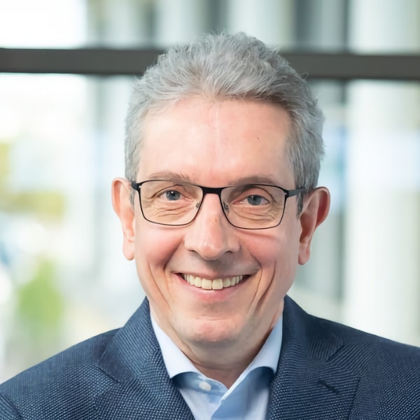 Headshot portrait of Bavarian robotics researcher Professor Wolfram Burgard, University of Technology Nuremberg, seen indoors, wearing a suit, smiling at the camera.