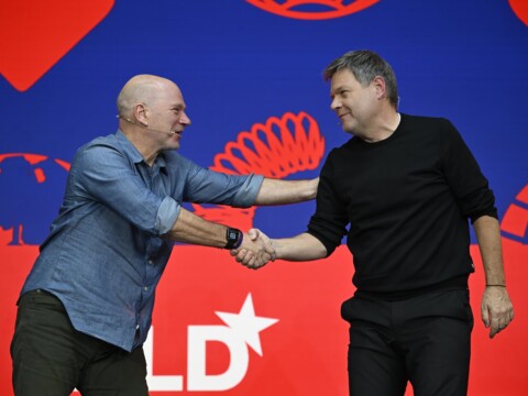 Economist Andrew McAfee (MIT Sloan School of Business) and German politician Robert Habeck (Green party) on stage at the DLD Munich conference, shaking hands.