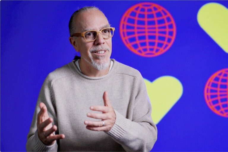 Astro Teller, head of Alphabet’s Moonshot Factory X, during an interview with DLD, sitting in a video studio, speaking in front of a blue screen showing the DLD Munich 2025 design: icons showing yellow hearts and red globes.