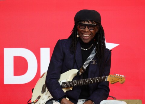 Legendary musician and producer Nile Rodgers on stage at the DLD Munich conference, laughing, holding his guitar.