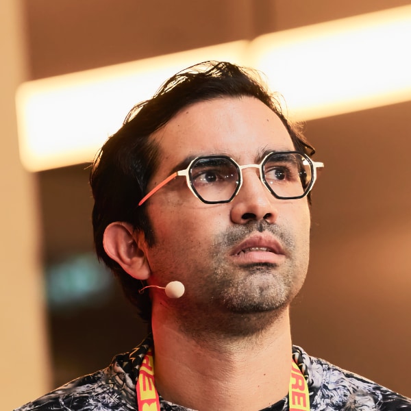 Portrait of Colombian artist Leo Castañeda, seen speaking at the DLD Munich conference, wearing a headset, looking to the right.