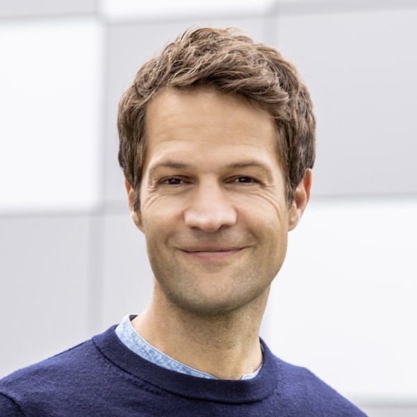 Headshot portrait of cell biologist Fabian Theis, Director Computational Health Center & Scientific Director of HelmholtzAI at Helmholtz Munich, smiling at the camera, photographed in front of a grey background.