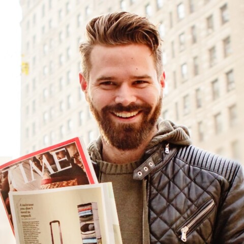 Outdoor portrait of entrepreneur Adrian Solgaard in front of a building, holding a copy of TIME magazine showing his company’s travel gear.