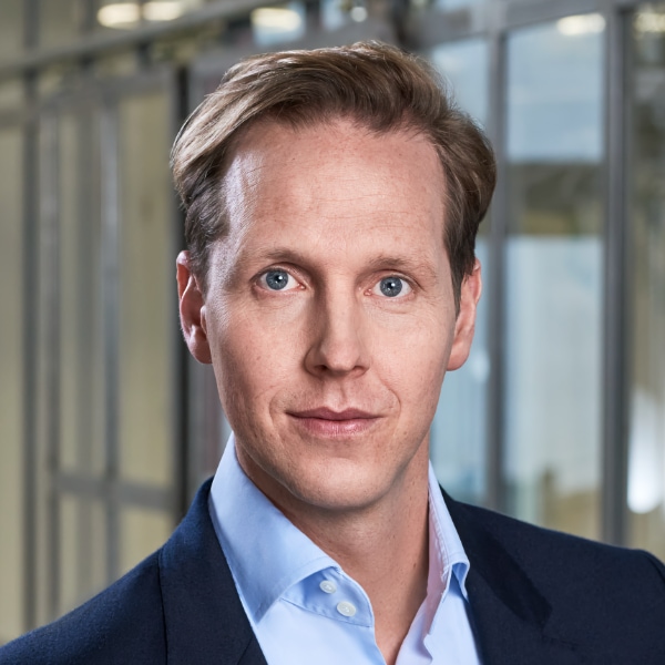 Headshot portrait of Johannes Rath, board member at Signal Iduna insurance, brightly lit in front of a striped background.