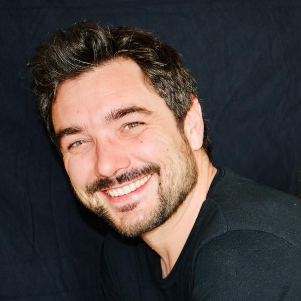 Headshot portrait of Julien Venne, MalsamaMind, smiling at the camera in front of a dark background.