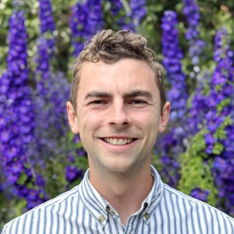 Headshot portrait of Mark Buckley, Programme Manager at the Ellen MacArthur Foundation, seen outdoors in front of colorful flowers.