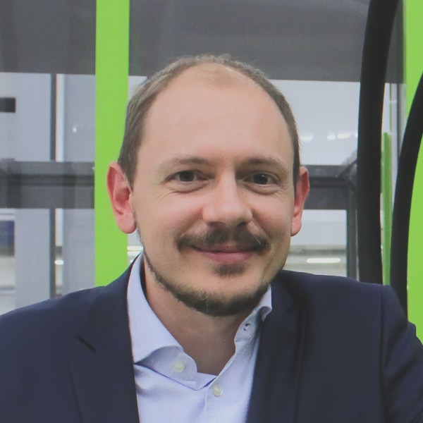Headshot portrait of Prof. Markus Sause, industrial automation specialist at University of Augsburg, seen in a lab setting with green and black metal structures behind him.