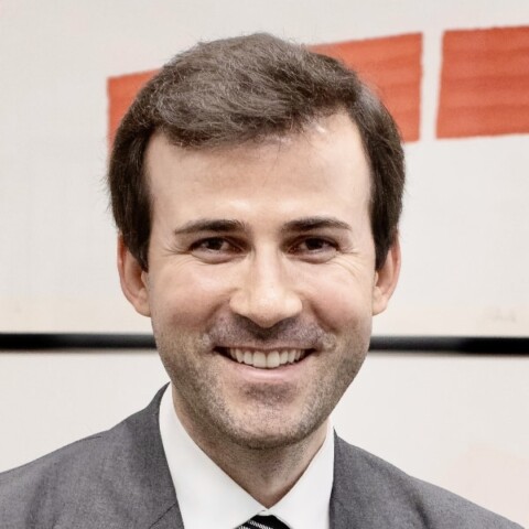 Headshot portrait of Uljan Sharka, founder and CEO of Domyn, in front of a red and white painting.