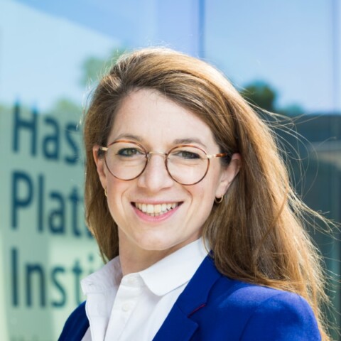 Headshot portrait of Dr. Ariel Dora Stern, digital health expert, standing in front of a logo of the at the Hasso Plattner Institute visible in the background.