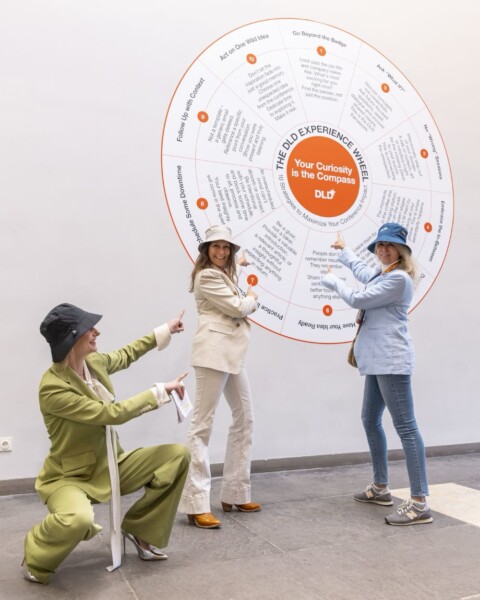 Female attendees of the DLD Future Hub conference pointing to a circular poster on the wall.