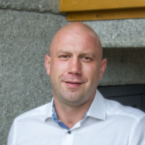 Environmental headshot portrait of Dean Domino Turzer, Oberland-K&auml;lte, in front of a wall.