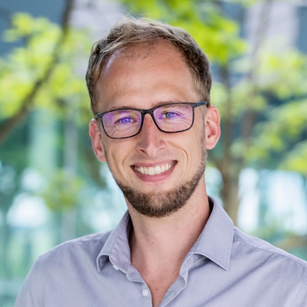 Headshot portrait of robotics researcher Jörn Vogel, DLR, seen outdoors in front of trees.