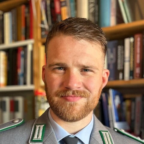 Headshot portrait of military expert Julian Werner, seen wearing a uniform in front of a bookshelf.